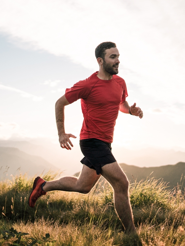 <p>Middle aged man running in a field of grass, surrounded by mountains.</p>
