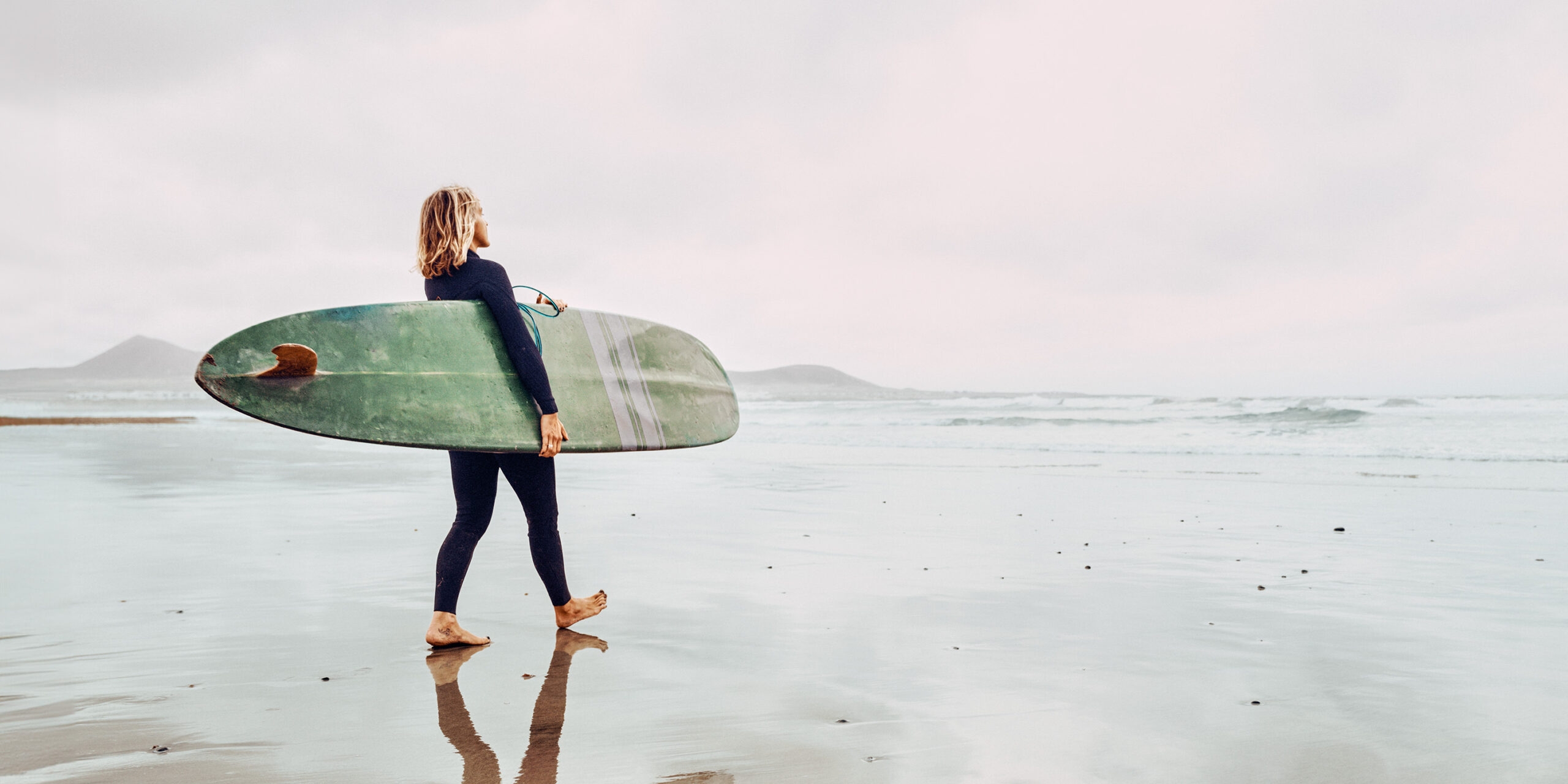 <p>Surfer woman with longboard surfboard at Famara beach in Lanzarote Canary Islands</p>